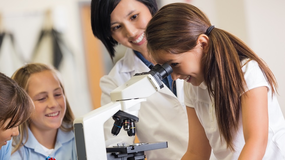 Excited elementary school girl using microscope in private science class